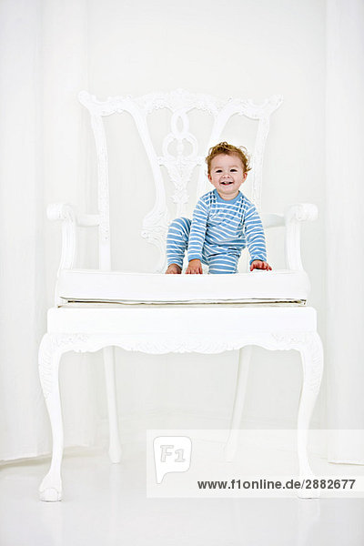 Baby Junge sitzt im Sessel und lächelt