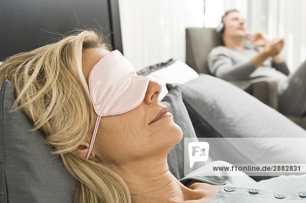 Frau mit Augenmaske und ihr Mann hört im Hintergrund Musik.