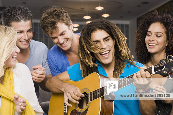Mann sitzt mit seinen Freunden und spielt Gitarre.