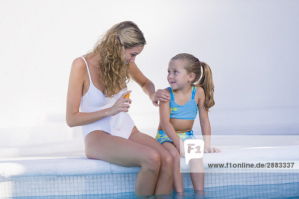 Frau mit ihrer Tochter am Pool sitzend