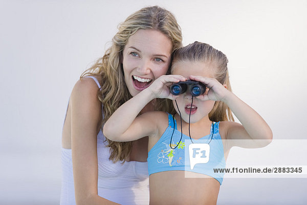Mädchen schaut mit lachender Mutter durchs Fernglas