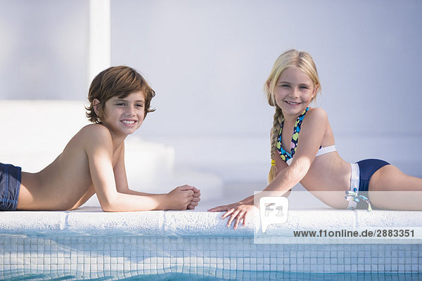 Junge mit einem Mädchen am Pool liegend und lächelnd