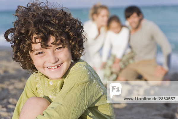 Junge lächelt mit seiner Familie am Strand.