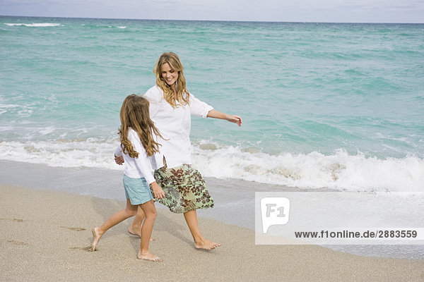 Frau  die mit ihrer Tochter am Strand spazieren geht.