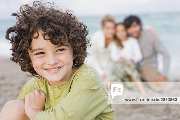 Junge lächelt mit seiner Familie am Strand.