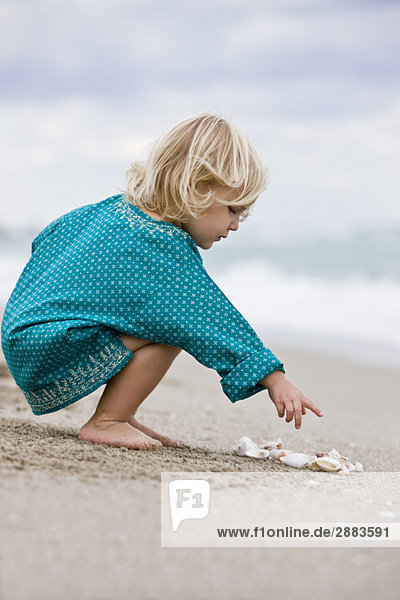Mädchen spielt mit Muscheln am Strand