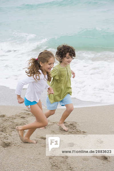 Ein Junge und ein Mädchen rennen am Strand.