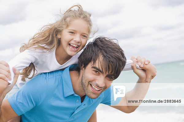 Man giving his daughter piggyback on the beach