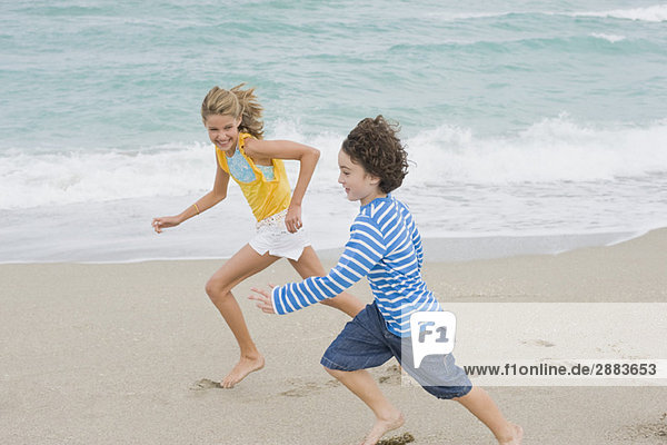 Ein Junge läuft mit einem Mädchen am Strand.