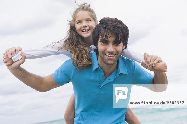 Man giving his daughter piggyback on the beach