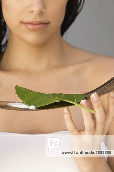 Woman holding a leaf and moisturizer on wooden tray