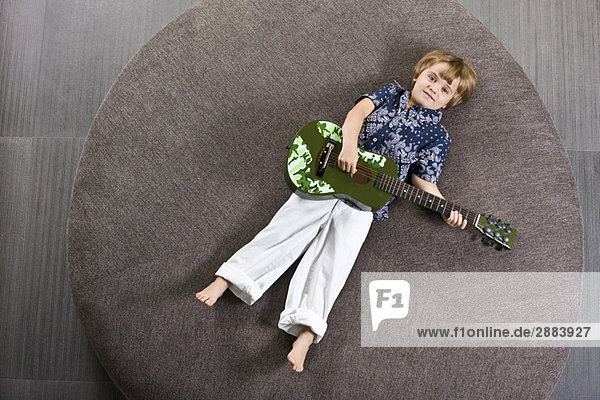 Junge auf einem runden Sofa liegend und Gitarre spielend