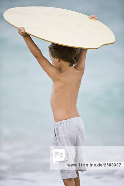 Rear view of a boy holding a body board over his head