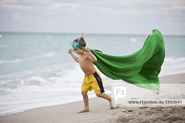 Junge  der eine Tauchermaske trägt und am Strand rennt.