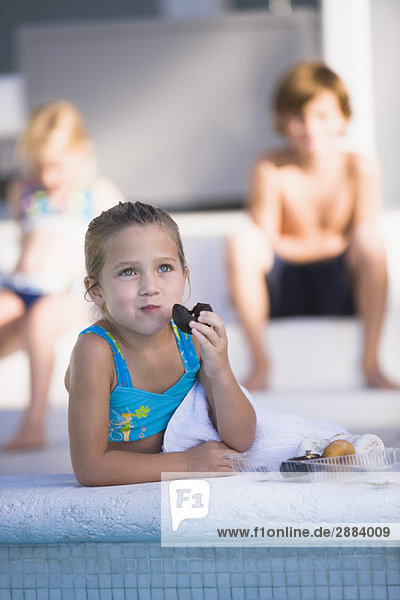 Mädchen essen Schoko-Donut am Pool