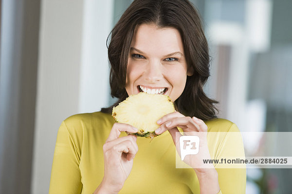 Porträt einer Frau beim Essen einer Ananasscheibe