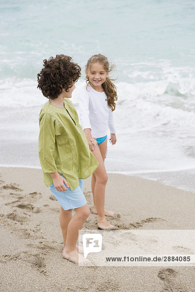 Ein Junge und ein Mädchen stehen mit Händchenhalten am Strand.