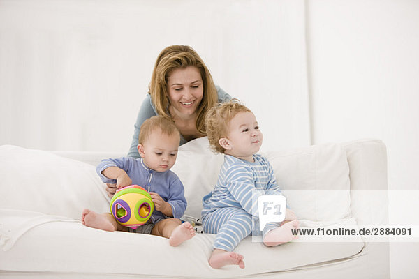 Frau spielt mit ihrem Sohn und ihrer Tochter auf einer Couch.