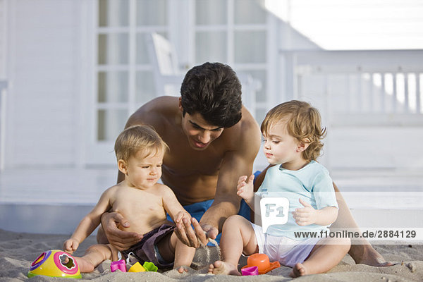Mann spielt mit seinem Sohn und seiner Tochter im Sand.