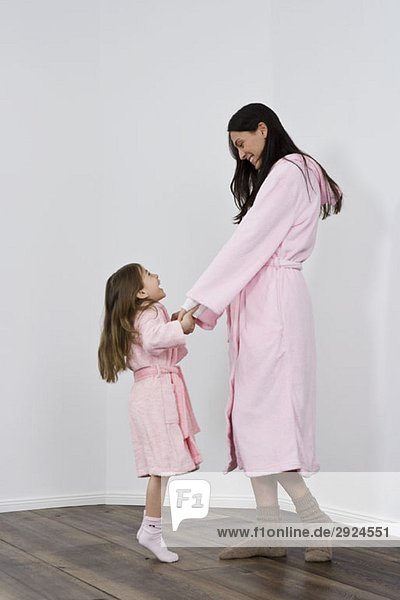 Eine Tochter und Mutter in rosa Bademänteln hält sich an den Händen.