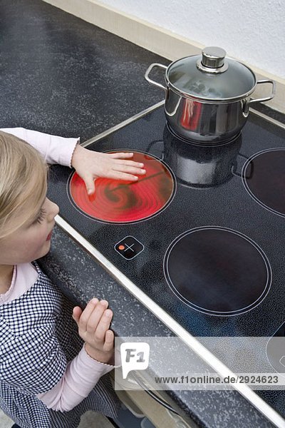 A young girl holding her hand over a hot electric stove burner