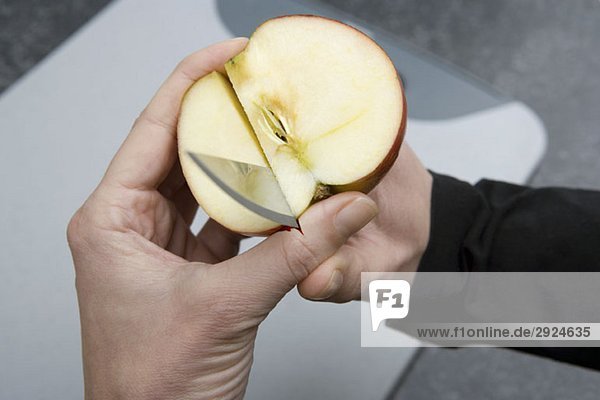 A person cutting through an apple and into their thumb