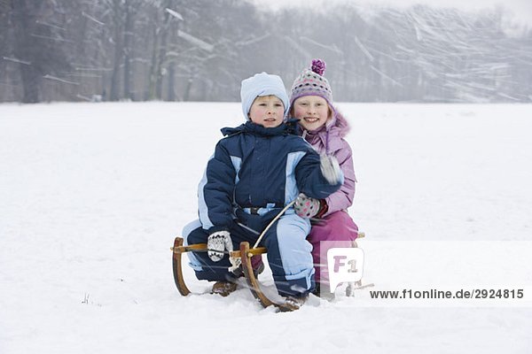 A brother and sister sitting on a sled together tobogganing