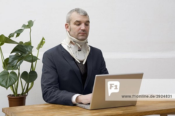 Ein Geschäftsmann mit einer Halskrause  der an einem Laptop arbeitet.