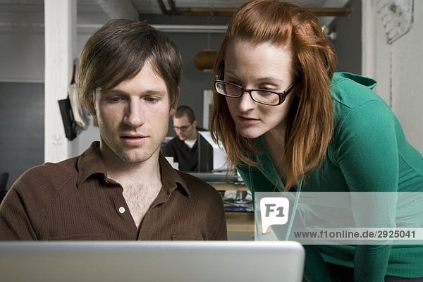 Ein Geschäftsmann und eine Geschäftsfrau,  die auf einen Laptop schauen.