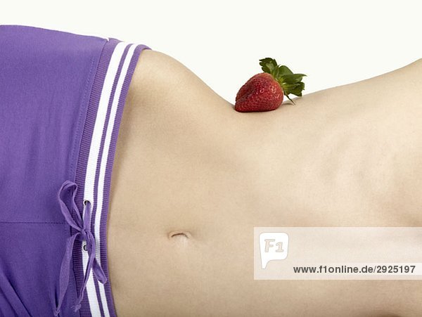 Mittelteil einer Frau  die eine Erdbeere auf ihrer Taille balanciert.