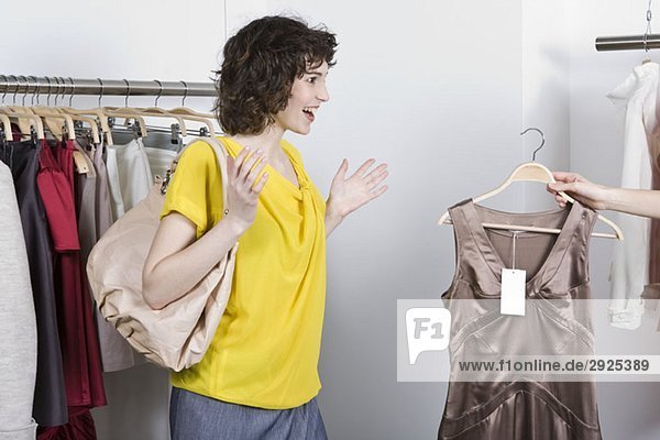 Eine Verkaufshilfe  die einer Frau ein Kleid in einem Geschäft zeigt.