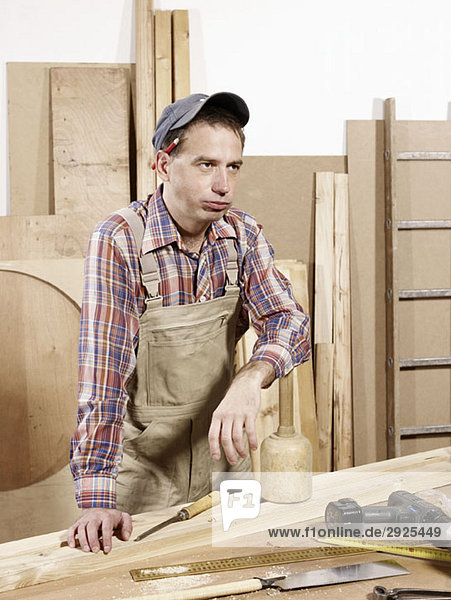 A tired man standing in a wood workshop