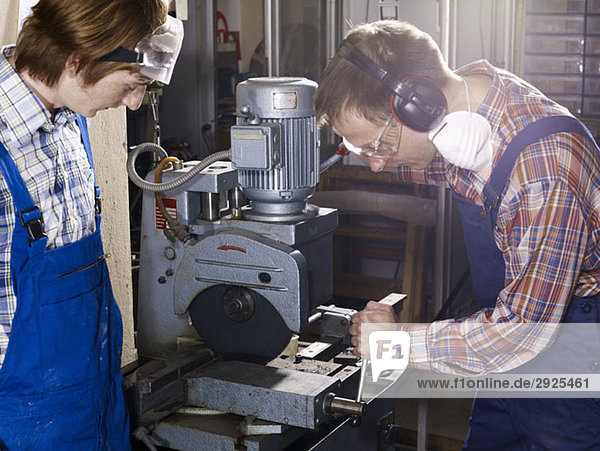 A man using an electric saw in a workshop while a young man looks on