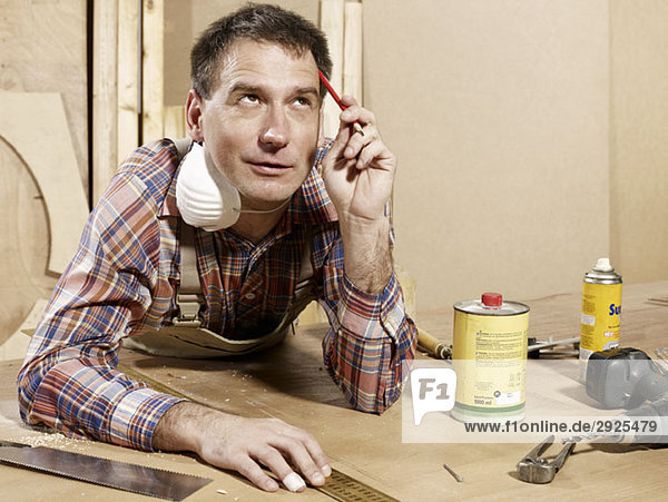 A man leaning on a workbench and thinking