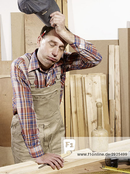 A man wiping his brow in a wood workshop
