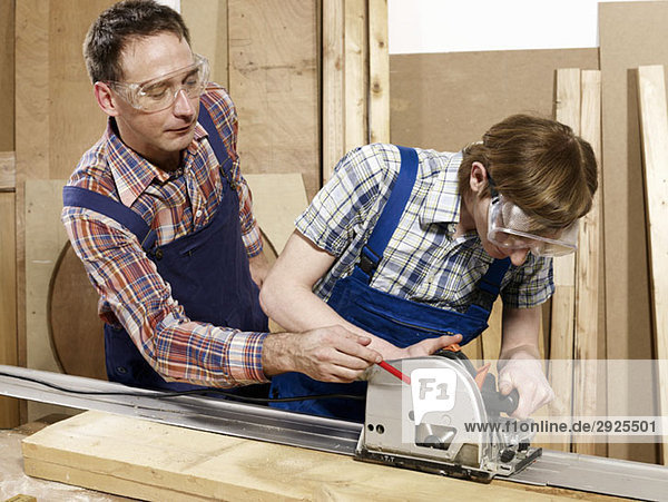 A man assisting a young man sawing wood