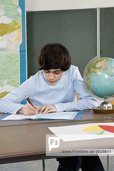 Ein Schuljunge  der an einem Schreibtisch arbeitet.