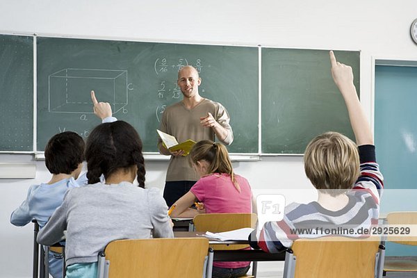 Rückansicht eines Schülers  der in einem Klassenzimmer die Hand hebt