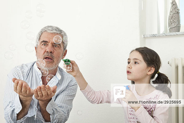 Ein Großvater und eine Enkelin spielen mit Seifenblasen.