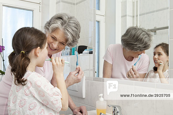 A grandmother helping her granddaughter brush her teeth
