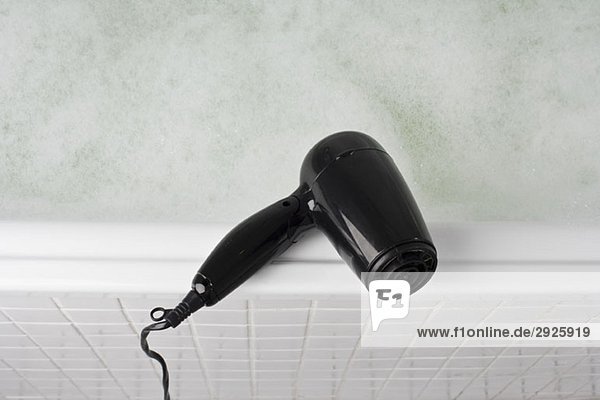 A hair dryer balancing on the edge of a full bathtub