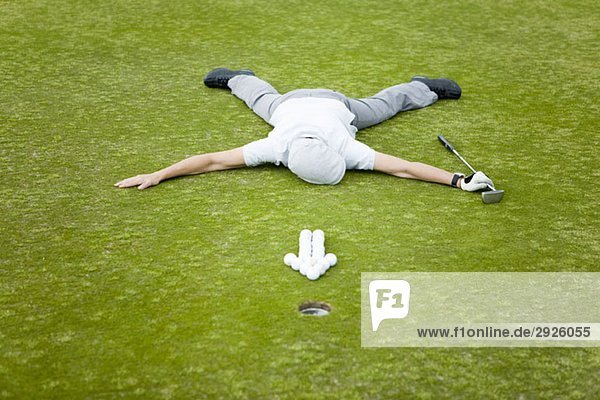 Ein Golfer  der auf einem Putting Green hinter einem Pfeil aus Golfbällen liegt.