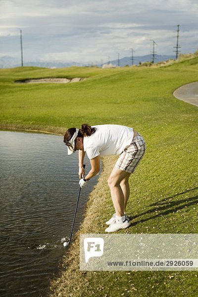Ein Golfer  der einen Golfball aus einer Wasserfalle sammelt.