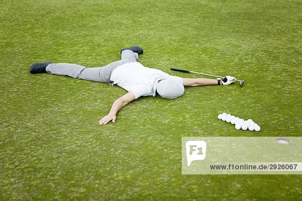 Ein Golfer  der auf einem Putting Green hinter einem Pfeil aus Golfbällen liegt.