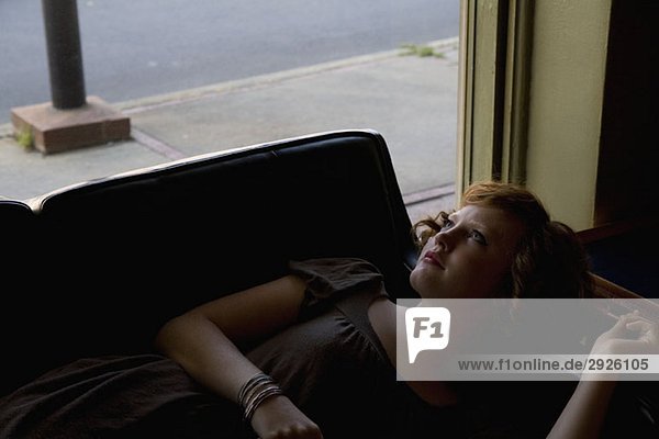 Eine junge Frau  die auf einem Sofa neben einem Fenster liegt.