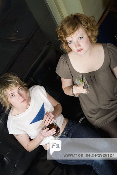 Zwei junge Frauen sitzen in einer Bar mit Getränken.