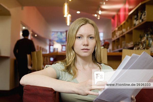 Eine junge Frau sitzt in einem Café und schaut sich die Speisekarte an.