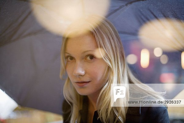 Eine junge Frau hält einen Regenschirm und schaut durch ein Fenster.