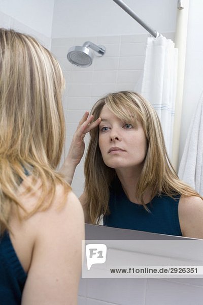 Eine junge Frau  die in einen Badezimmerspiegel schaut.