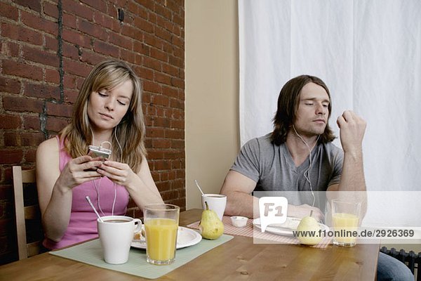 Ein junges Paar sitzt beim Frühstück und hört sich MP3-Player an.